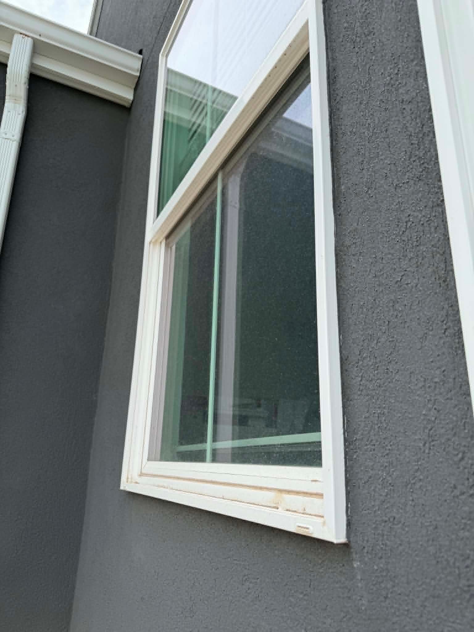 A second-storey window and gutter line on a grey stucco home after cleaning